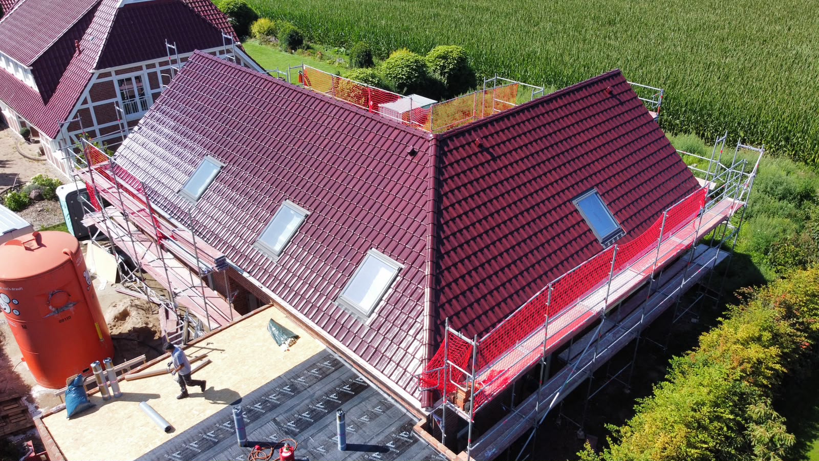 Luftaufnahme eines fertig gedeckten Dachs mit dunkelroten Dachziegeln und vier Dachflächenfenstern